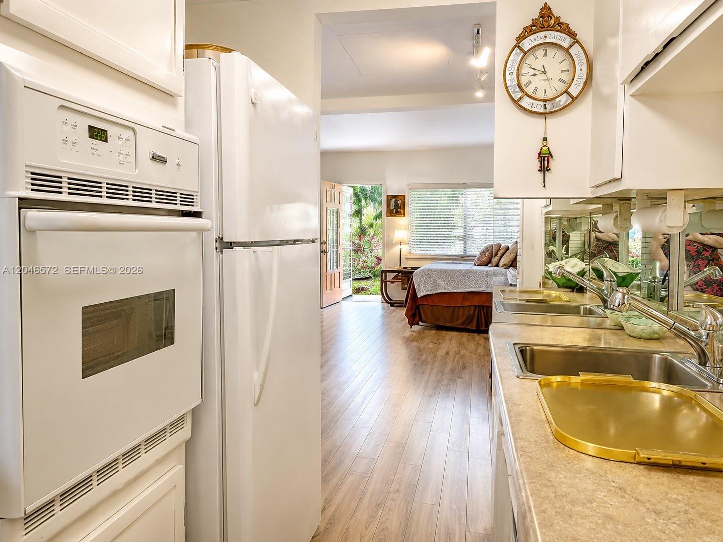 A white kitchen with a wall oven and refrigerator overlooks a bedroom with wood flooring — 1050 Pennsylvania Ave # A, Miami Beach FL 33139, MIAMI BEACH, FL