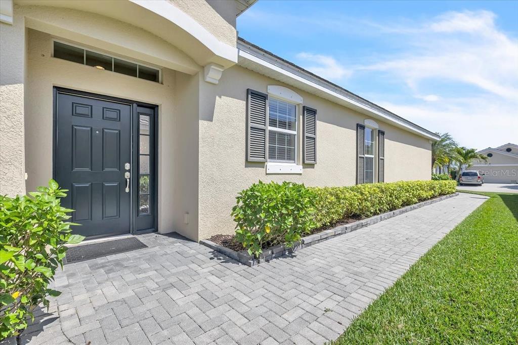 A paved walkway leads to the front entrance of a house with a dark door — 2615 VAREO COURT, CAPE CORAL, FL