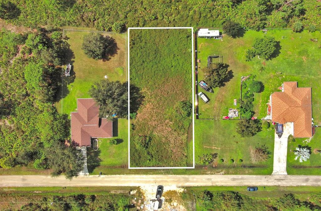 An aerial view shows a rectangular vacant lot situated between two residential properties — 1413 5TH AVENUE, LEHIGH ACRES, FL