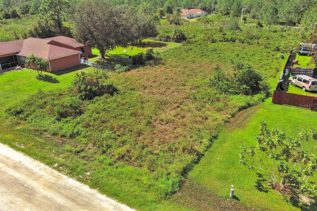 An aerial view shows a vacant, overgrown lot situated between two residential properties — 1413 5TH AVENUE, LEHIGH ACRES, FL