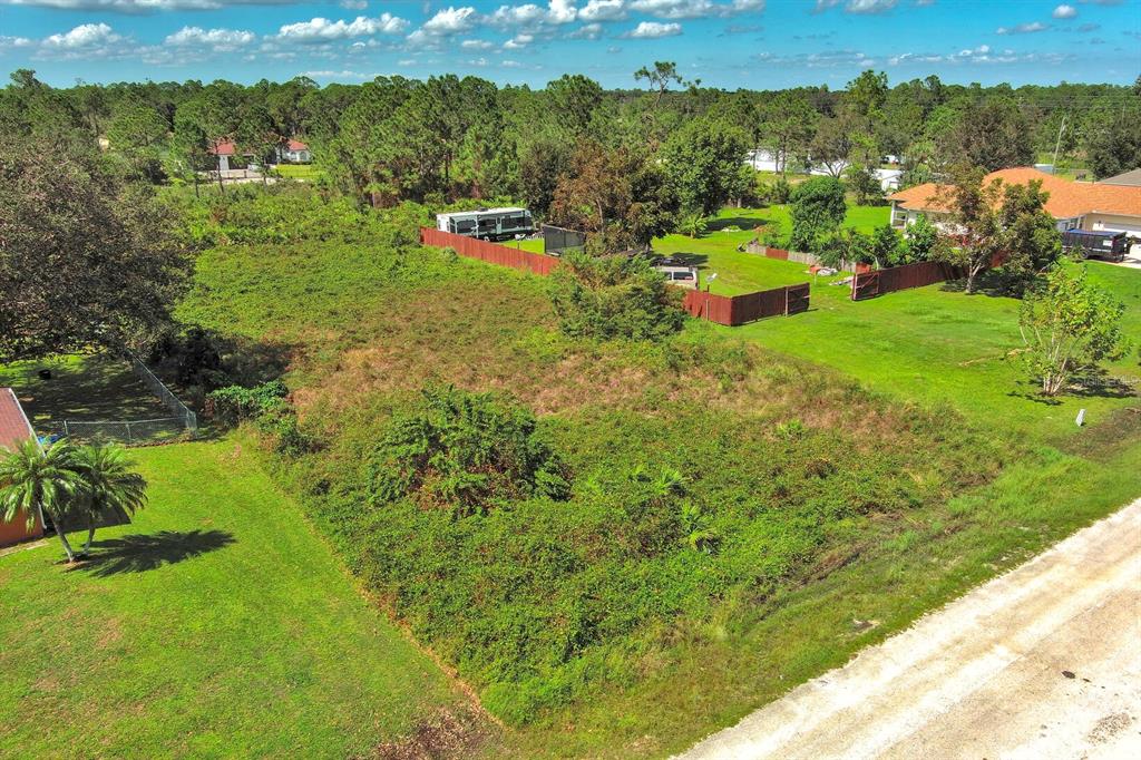 An aerial view shows a vacant, overgrown lot bordered by a dirt road and fences — 1413 5TH AVENUE, LEHIGH ACRES, FL