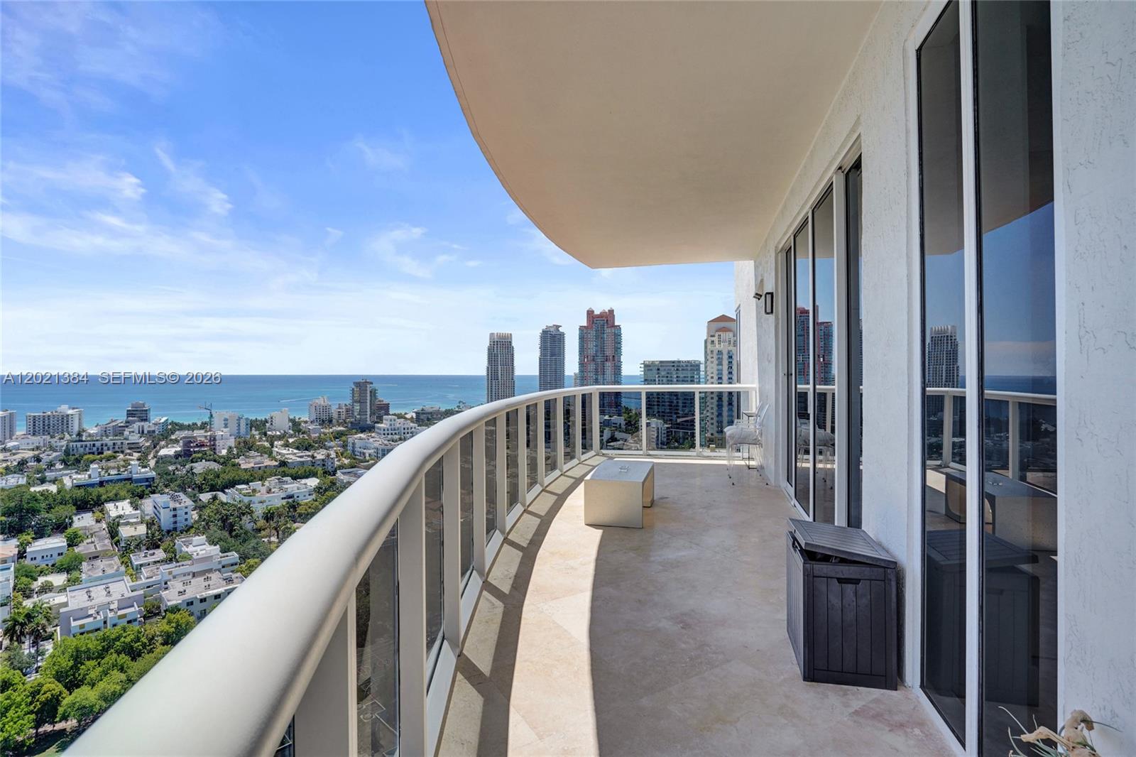 A curved balcony with stone flooring overlooks a city skyline and the ocean — 400 Alton Rd, Miami Beach FL 33139, MIAMI BEACH, FL