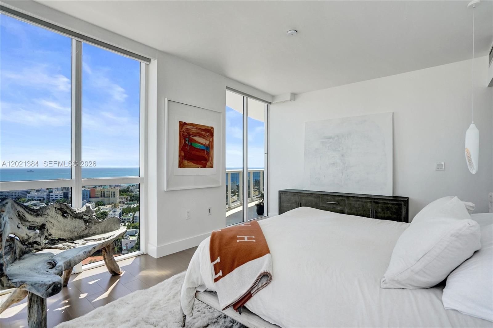 A bedroom features floor-to-ceiling windows with ocean views, a white bed, and driftwood furniture — 400 Alton Rd, Miami Beach FL 33139, MIAMI BEACH, FL