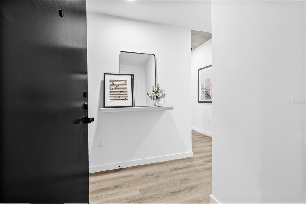 A modern entryway features a black door, a floating shelf with decor, and wood flooring — 221 MAIN STREET N UNIT B4-1115, ST PETERSBURG, FL
