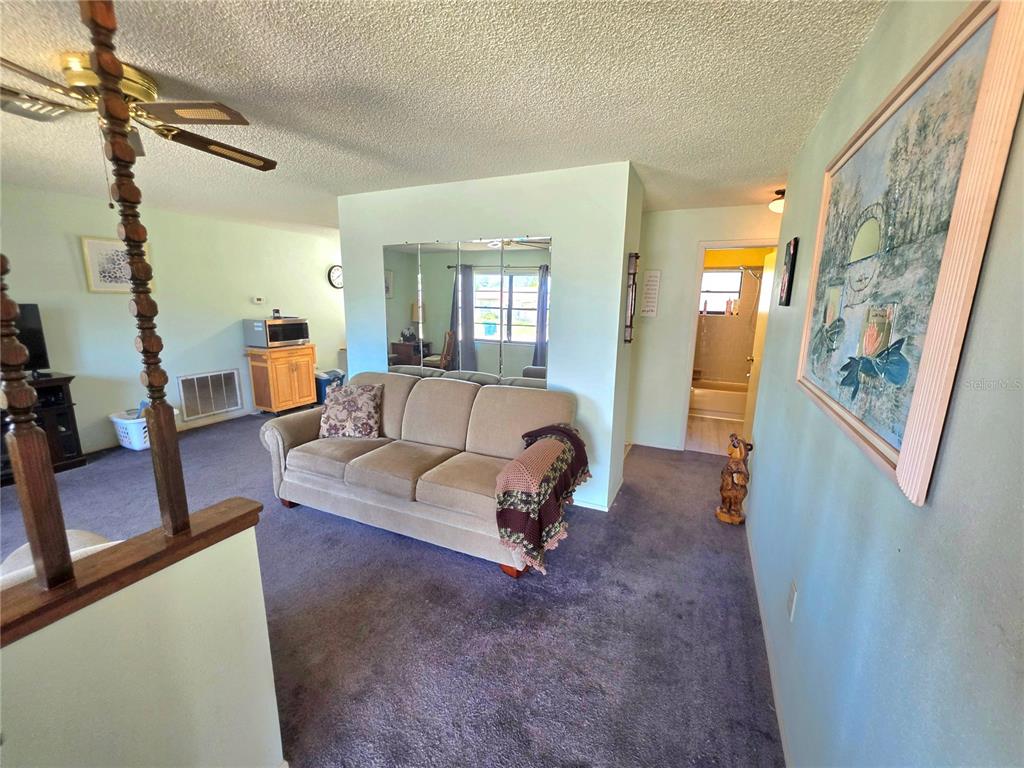 A living room features a beige sofa, purple carpeting, and a mirrored wall partition — 6402 COVEWOOD DRIVE, SPRING HILL, FL