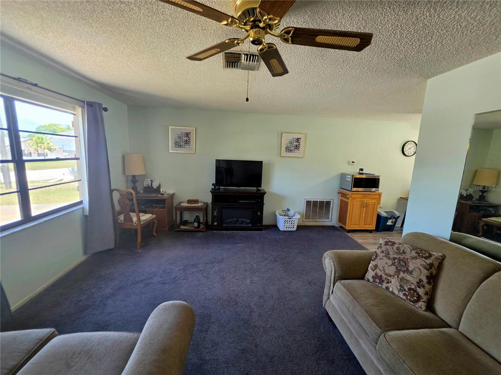 A living room features dark carpeting, a ceiling fan, a television, and a desk area — 6402 COVEWOOD DRIVE, SPRING HILL, FL