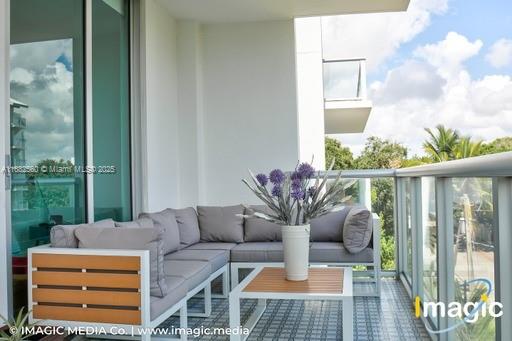 A modern balcony features a gray sectional sofa, a small wooden table, and a potted plant — 720 NE 62nd St # 402, Miami FL 33138, MIAMI, FL