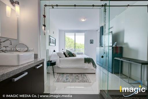 A modern bathroom with a vessel sink overlooks a bedroom through a glass sliding door — 720 NE 62nd St # 402, Miami FL 33138, MIAMI, FL