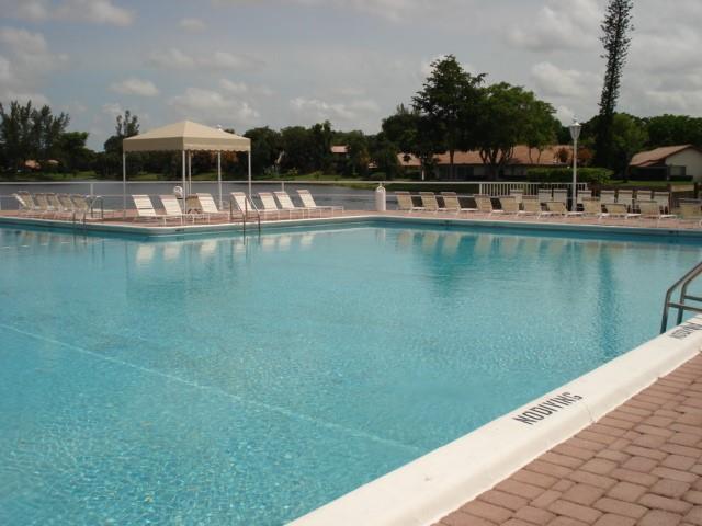A large outdoor swimming pool with lounge chairs and a covered cabana near a lake — 3740 Inverrary Drive # 1a, Lauderhill FL 33319, LAUDERHILL, FL
