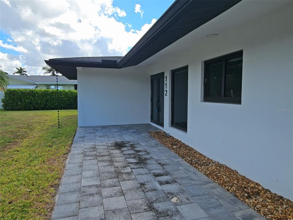 A paved patio area sits beside a white house with a dark roof and trim — 112 BAYSHORE DRIVE, CAPE CORAL, FL