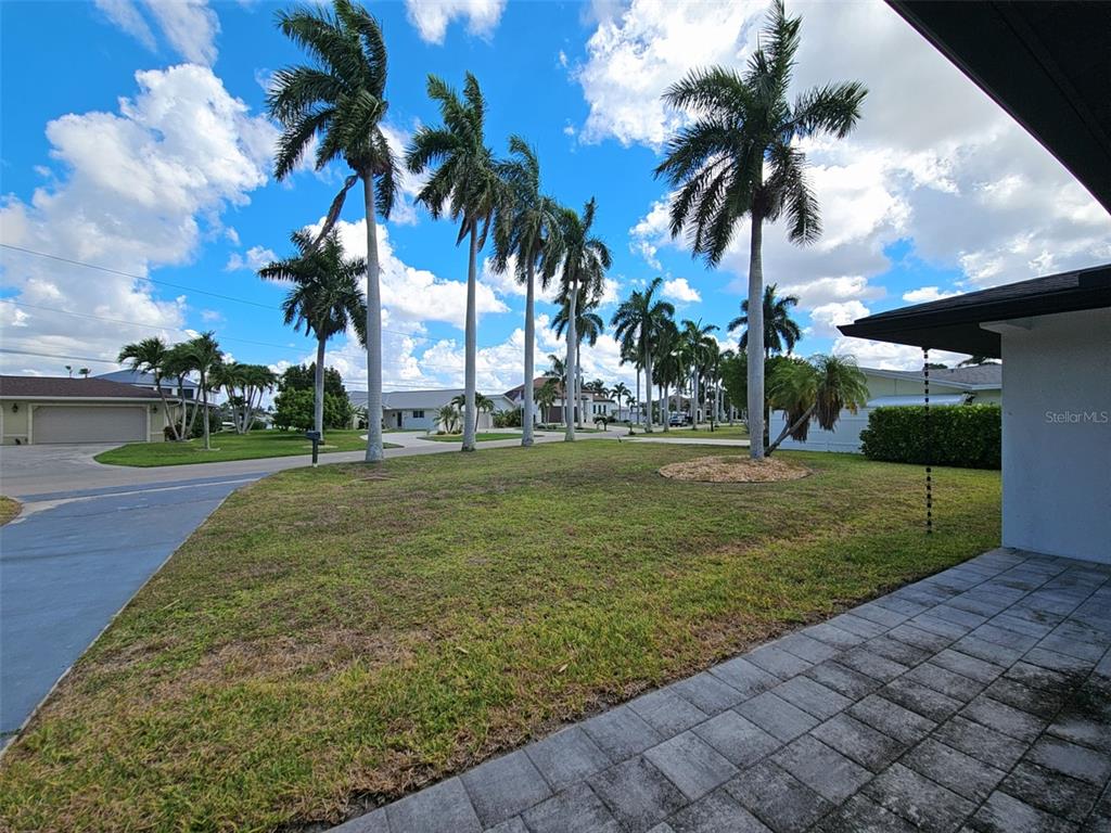 A grassy front yard features several tall palm trees under a blue sky with clouds — 112 BAYSHORE DRIVE, CAPE CORAL, FL