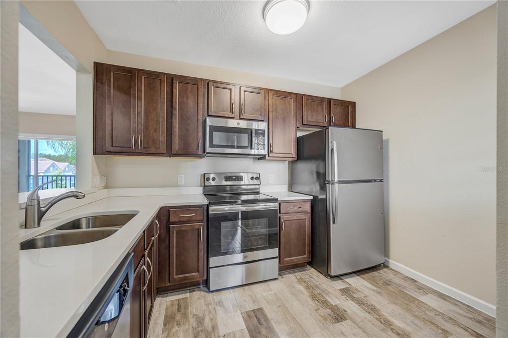 A kitchen features dark wood cabinets, stainless steel appliances, white countertops, and wood-look flooring — 1231 GODAVARI WAY UNIT 203, WESLEY CHAPEL, FL