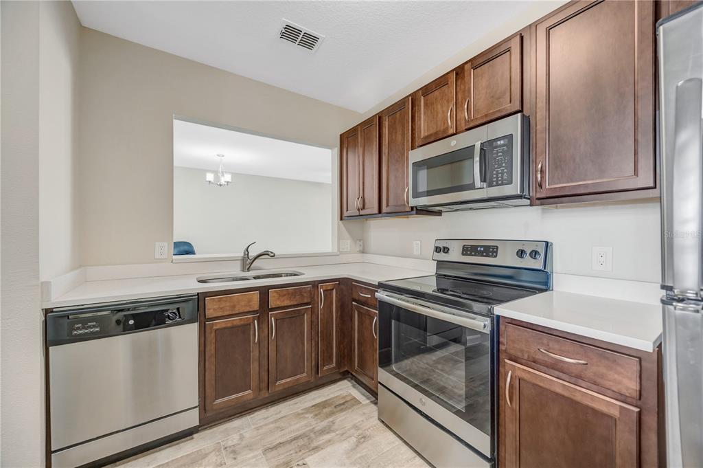 A kitchen with dark wood cabinets, stainless steel appliances, and white countertops — 1231 GODAVARI WAY UNIT 203, WESLEY CHAPEL, FL
