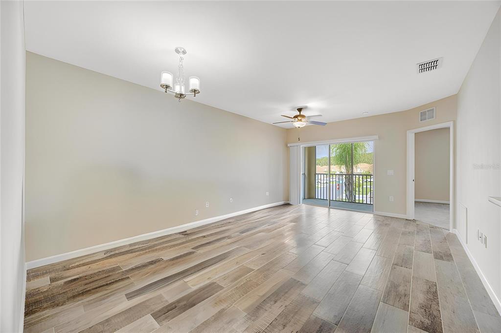 An empty living room features wood-look tile flooring, a ceiling fan, and a sliding glass door — 1231 GODAVARI WAY UNIT 203, WESLEY CHAPEL, FL