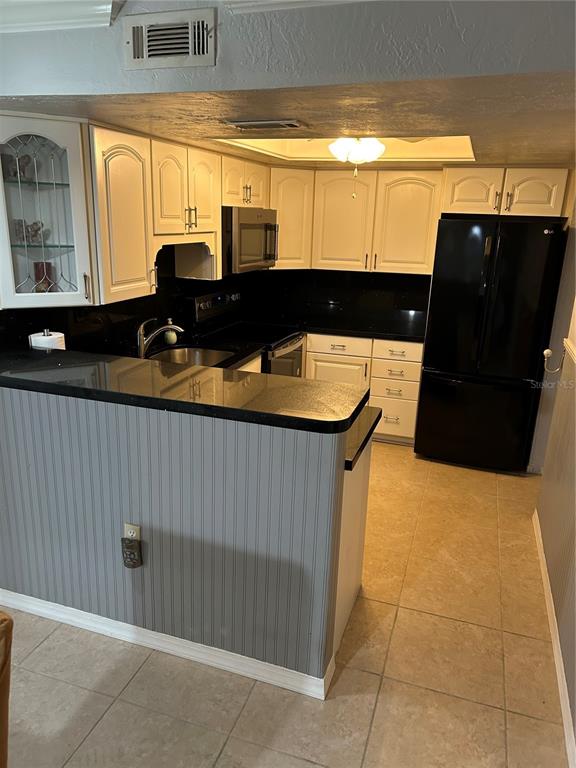 A kitchen features white cabinets, black countertops, a black refrigerator, and light-colored tile flooring — 1505 LENNOX ROAD E UNIT 1505, PALM HARBOR, FL