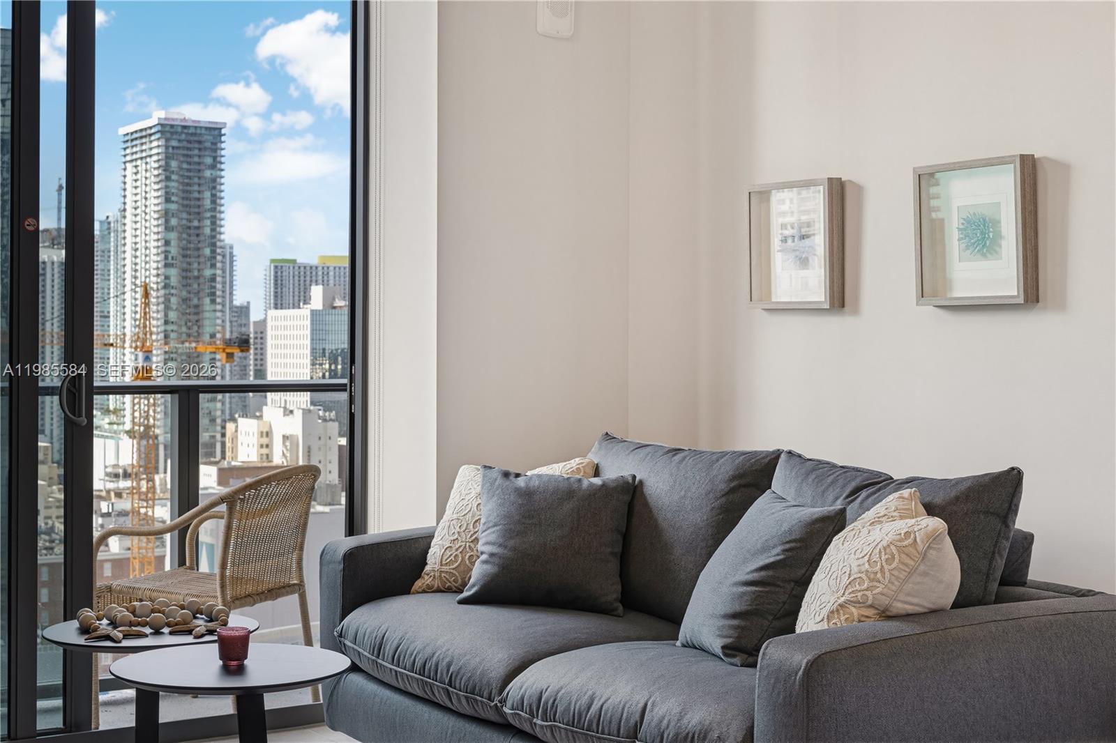 A grey sofa sits in a living room with a view of city skyscrapers — 121 NE 5th # 2604, Miami FL 33132, MIAMI, FL
