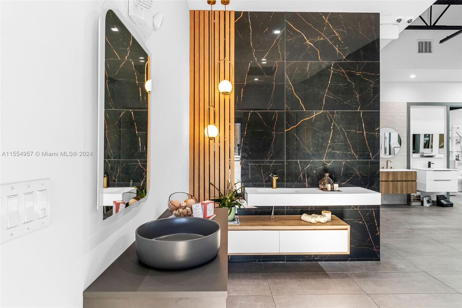 This bathroom showroom features a black marble accent wall, wooden slats, and modern vanity sinks — Bath Vanities/Accessories and Flooring, Doral FL 33122, DORAL, FL