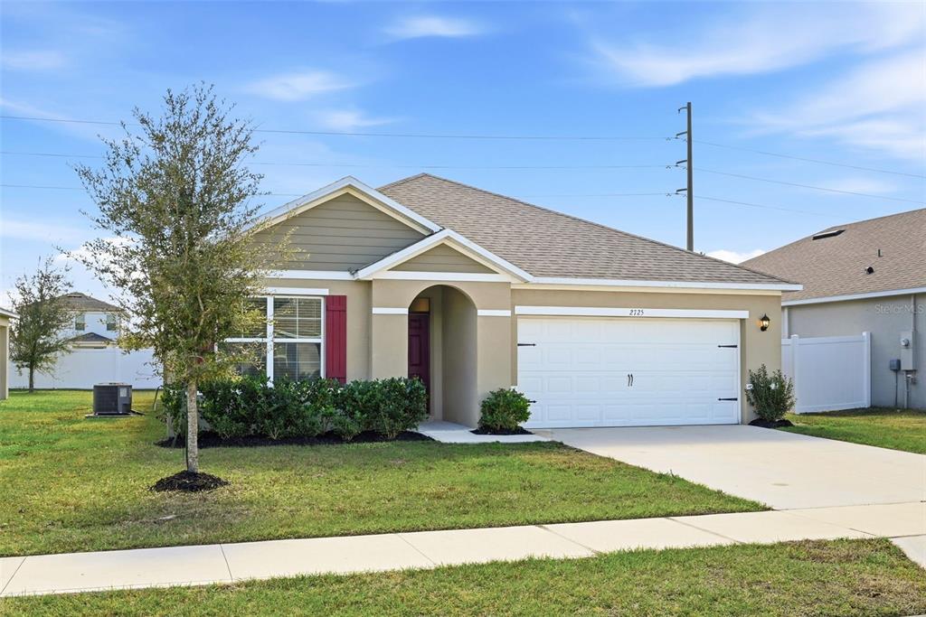 A single-story suburban house with a tan exterior, a two-car garage, and a front lawn — 2725 DUMONT LANE, TAVARES, FL