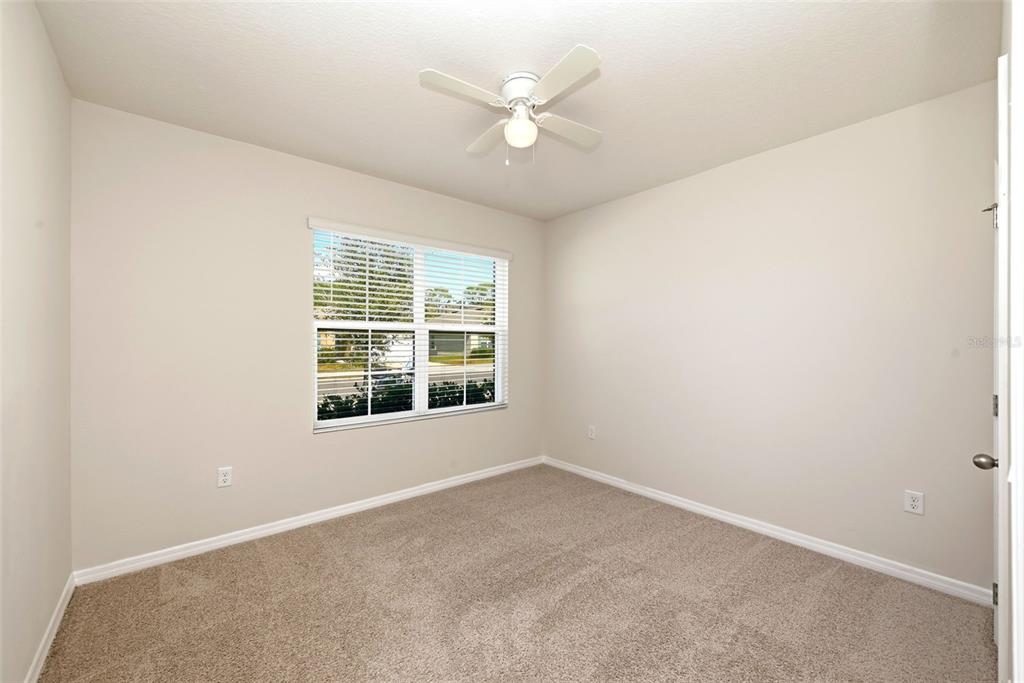 An empty bedroom with beige walls, tan carpet, a ceiling fan, and a window with blinds — 2725 DUMONT LANE, TAVARES, FL