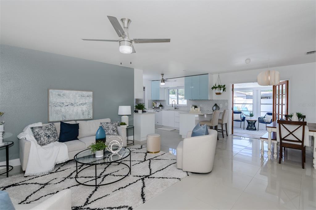 An open-concept living room and kitchen feature white tile floors, a gray accent wall, and furniture — 1435 77TH AVENUE N, ST PETERSBURG, FL