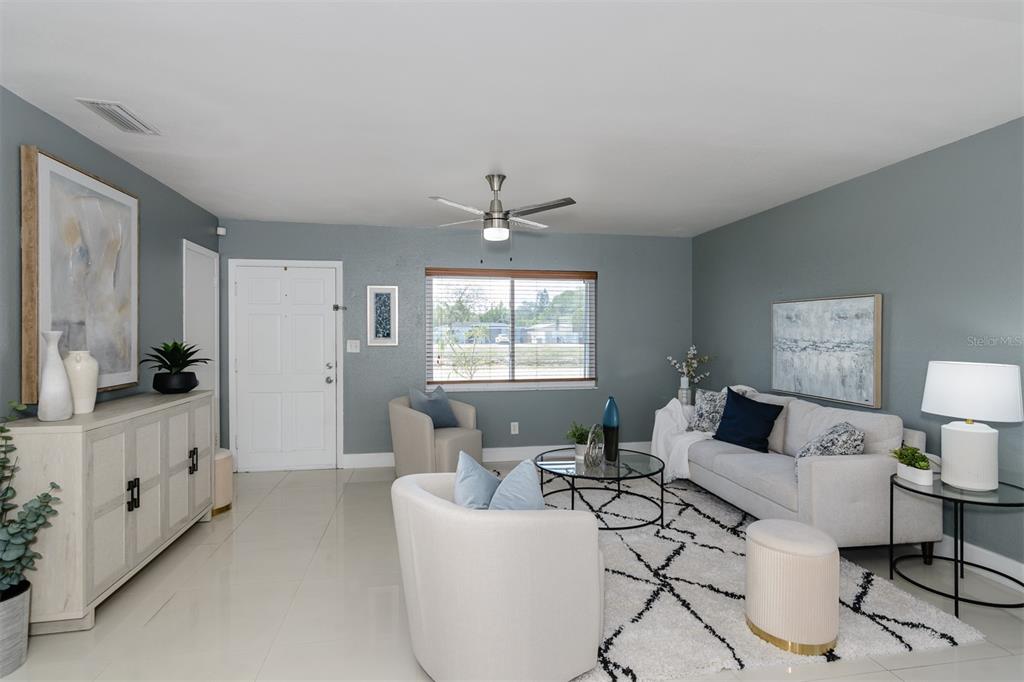 A living room features light blue walls, tile flooring, a white sofa, and a ceiling fan — 1435 77TH AVENUE N, ST PETERSBURG, FL