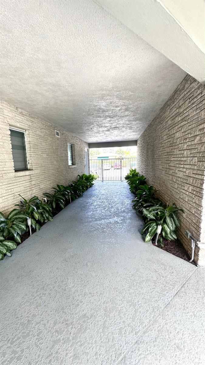A covered walkway features textured stone walls, a concrete floor, and potted plants — 414 Seasage Drive # 0030, Delray Beach FL 33483, DELRAY BEACH, FL