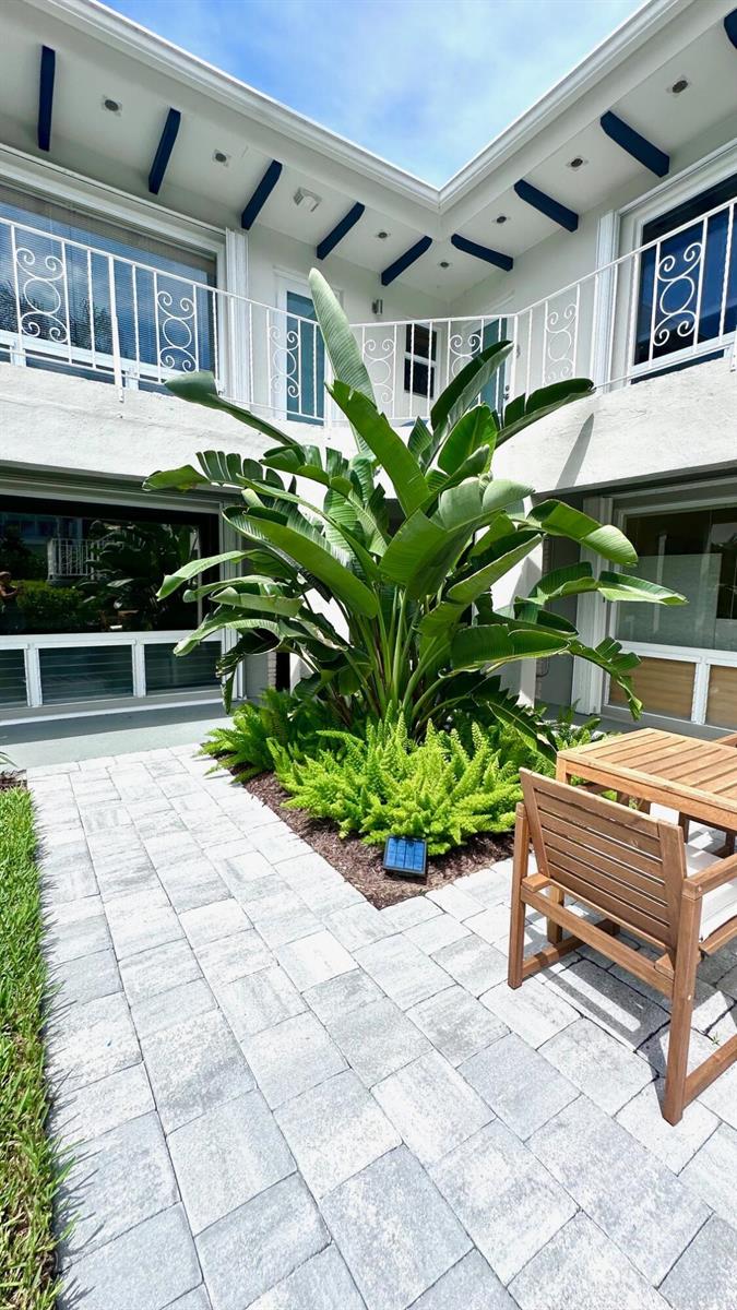 A courtyard features a large bird of paradise plant, ferns, and a wooden patio set — 414 Seasage Drive # 0030, Delray Beach FL 33483, DELRAY BEACH, FL
