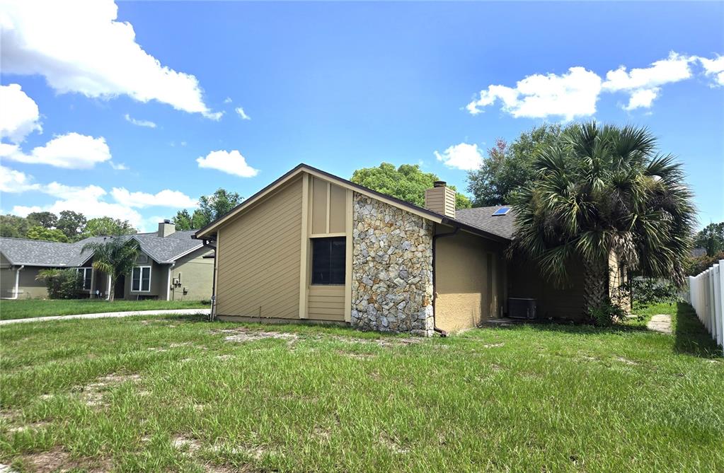 A side view of a house featuring tan siding, a stone chimney, and a palm tree — 8422 MARGARITA DRIVE, ORLANDO, FL