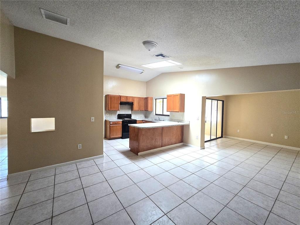 An open-concept kitchen with wood cabinets and a breakfast bar overlooks a tiled living area — 8422 MARGARITA DRIVE, ORLANDO, FL