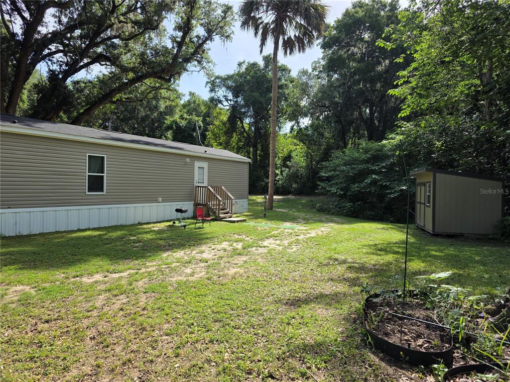 The exterior of a mobile home features tan siding, a small wooden deck, and a shed — 5160 NW 190TH PLACE, REDDICK, FL