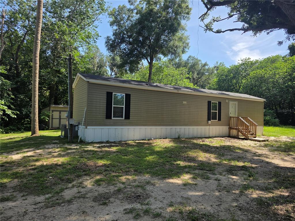 A tan mobile home with black shutters and a wooden staircase sits on a dirt lot — 5160 NW 190TH PLACE, REDDICK, FL