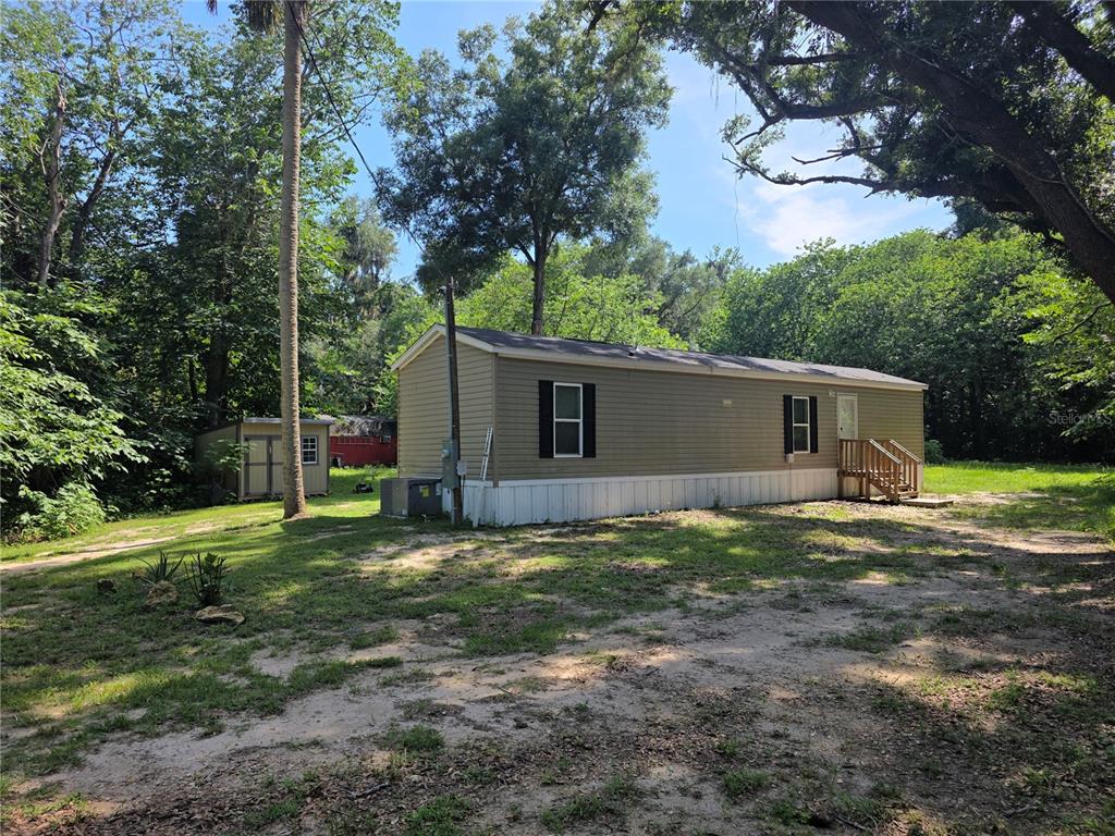 A tan mobile home sits on a grassy lot with a shed and trees nearby — 5160 NW 190TH PLACE, REDDICK, FL