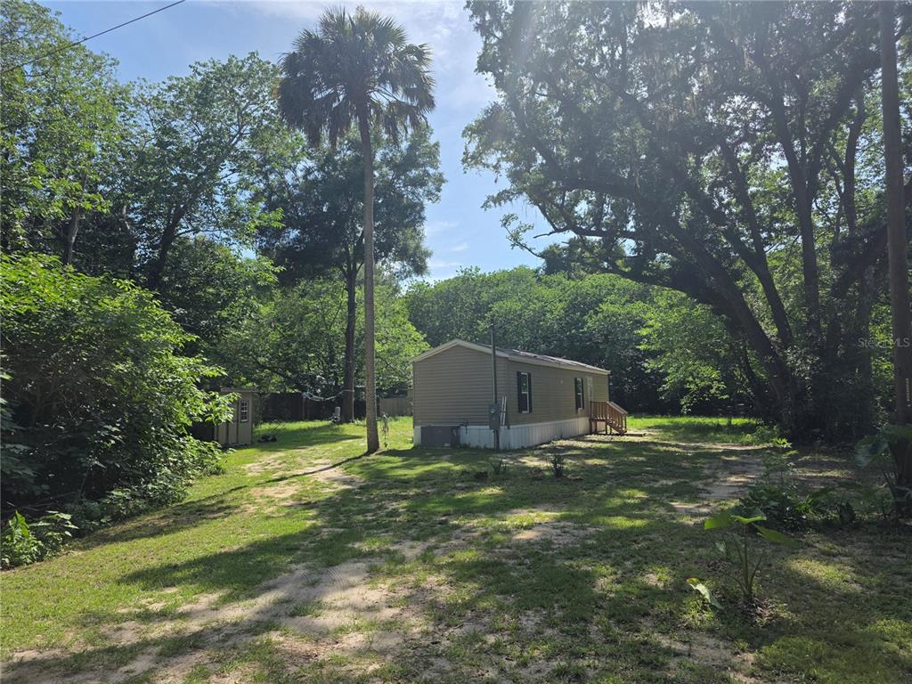 A single-wide mobile home sits on a grassy, wooded lot with a small storage shed — 5160 NW 190TH PLACE, REDDICK, FL