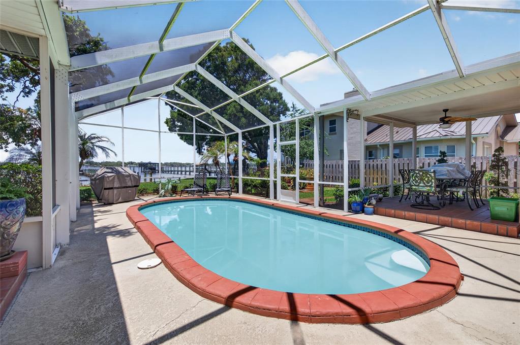 A screened-in patio features an oval swimming pool with a red brick coping — 1209 N HALIFAX AVENUE, DAYTONA BEACH, FL