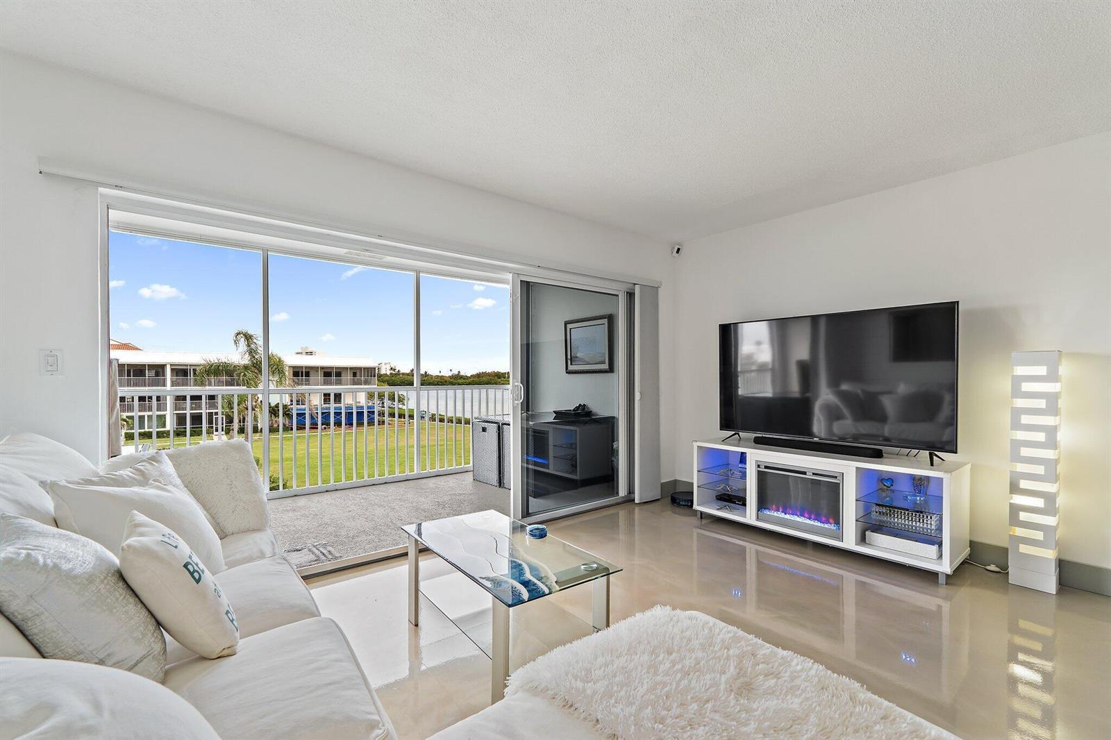 A living room features white furniture, a glass coffee table, and a sliding door to a balcony — 100 Waterway Road # E305, Tequesta FL 33469, TEQUESTA, FL