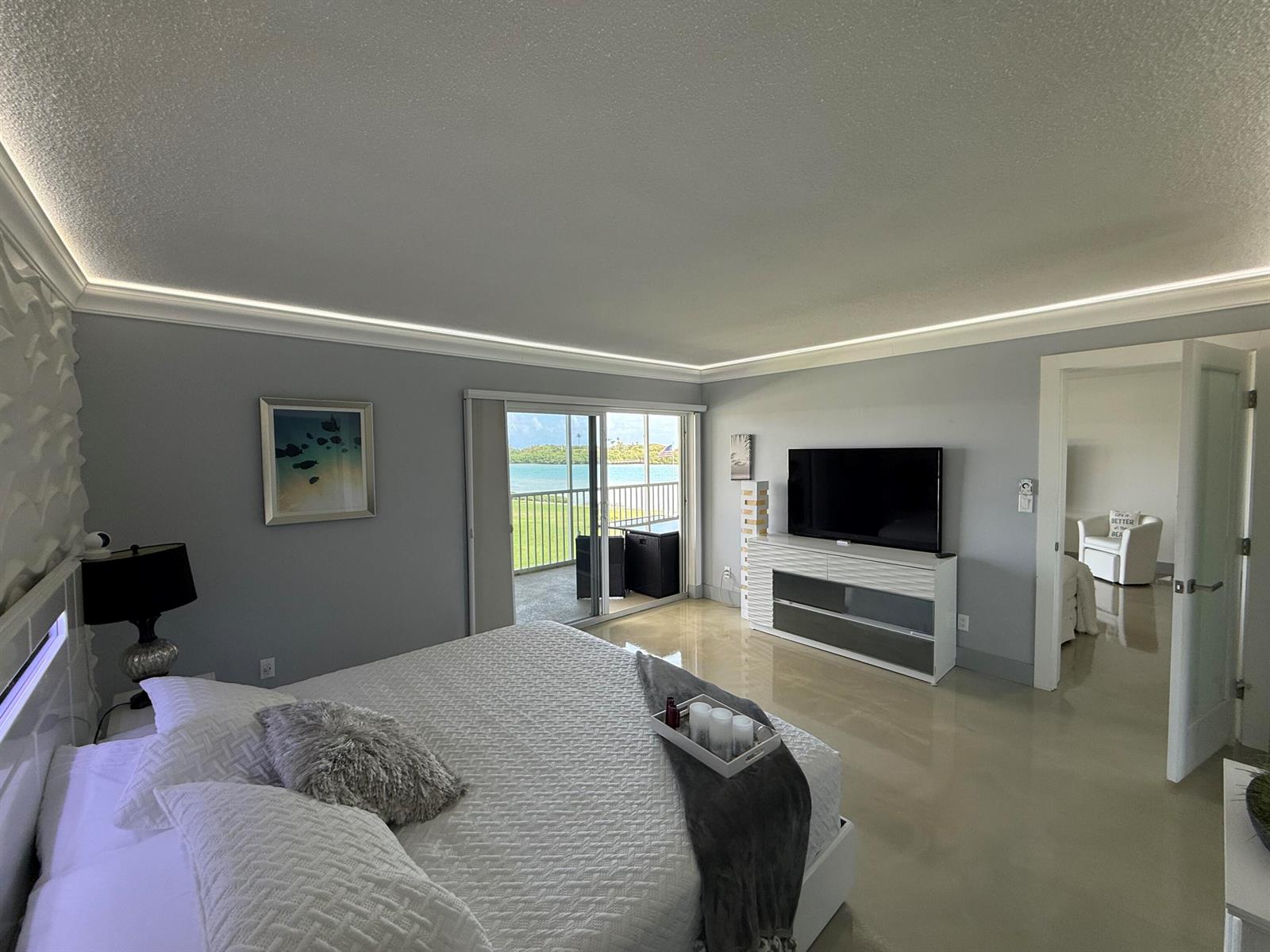 A bedroom with a king bed, television console, and sliding glass doors leading to a balcony — 100 Waterway Road # E305, Tequesta FL 33469, TEQUESTA, FL