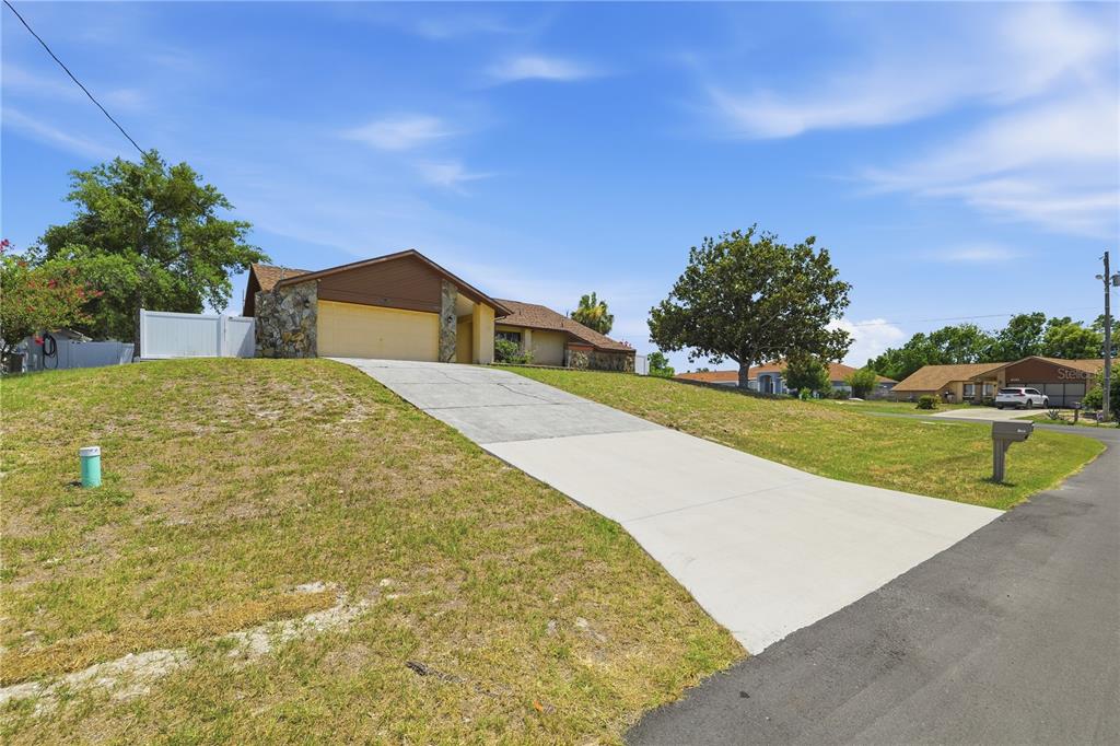 A single-story house with a two-car garage and a concrete driveway on a grassy hill — 9470 MONTEBELLO LANE, SPRING HILL, FL