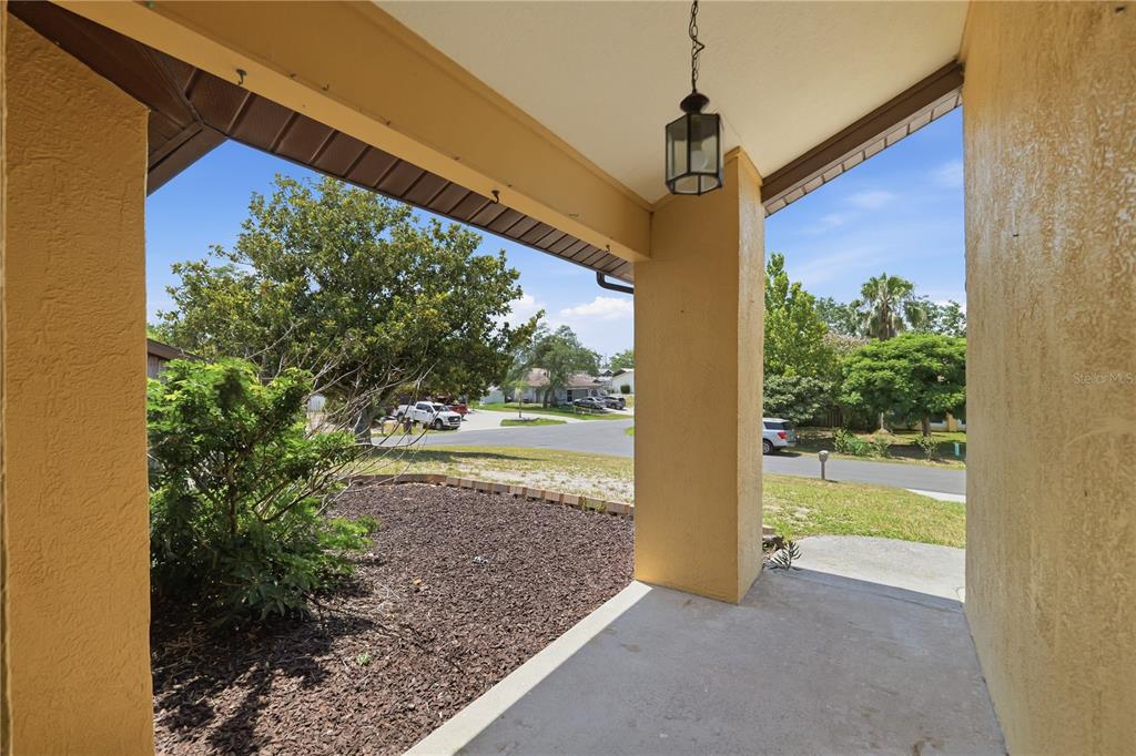 A covered concrete front porch overlooks a suburban street with trees and parked cars — 9470 MONTEBELLO LANE, SPRING HILL, FL