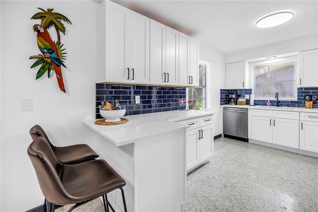 A kitchen features white cabinets, a dark blue tile backsplash, and a white breakfast bar — 3518 POCAHONTAS DRIVE, LARGO, FL