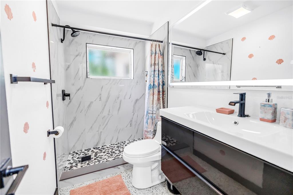 A bathroom features a walk-in shower with marble-look tile, a toilet, and a modern vanity — 3518 POCAHONTAS DRIVE, LARGO, FL