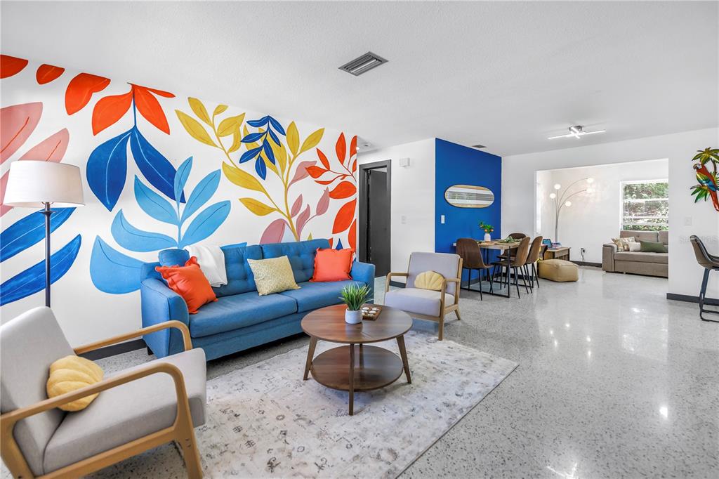 A living room features a colorful leaf mural, a blue sofa, and polished concrete floors — 3518 POCAHONTAS DRIVE, LARGO, FL