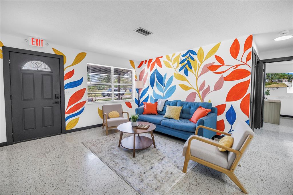 A living room features a blue sofa, two armchairs, and a colorful leaf-patterned wall mural — 3518 POCAHONTAS DRIVE, LARGO, FL
