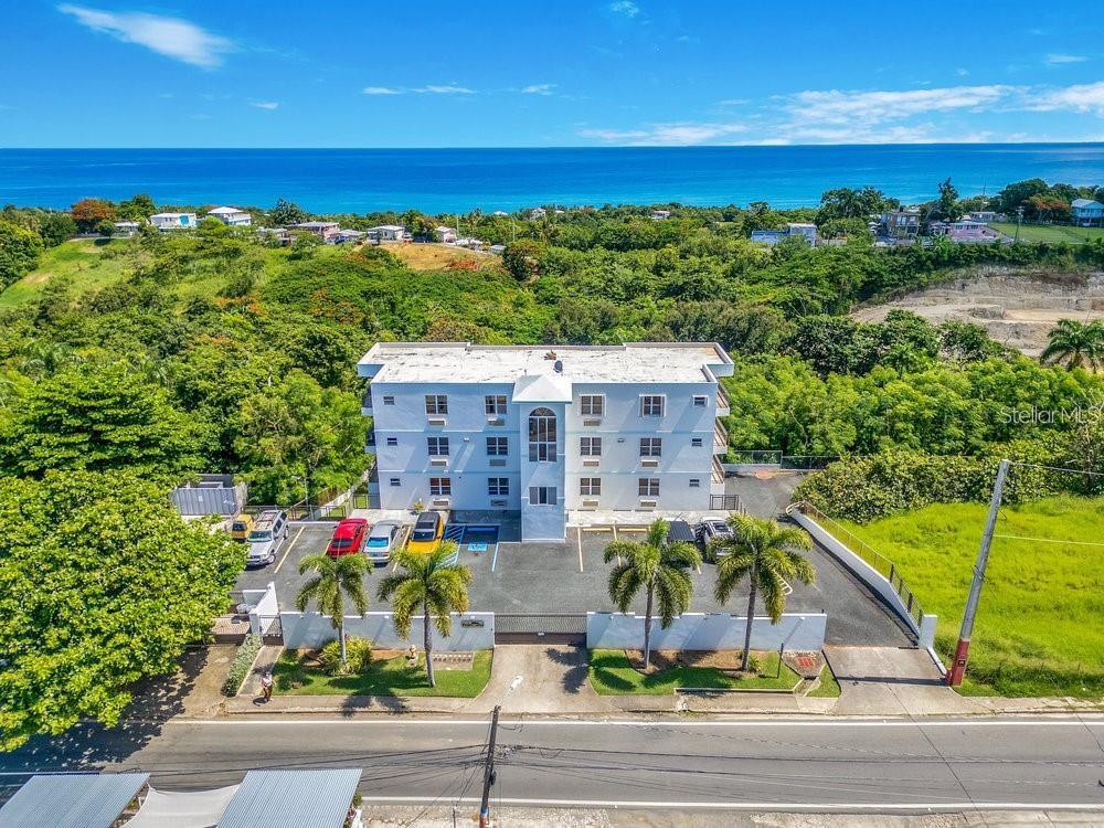 An aerial view of a four-story white apartment building with a parking lot and ocean views — 413 CAM. CARRETAS UNIT A7, RINCON, PR
