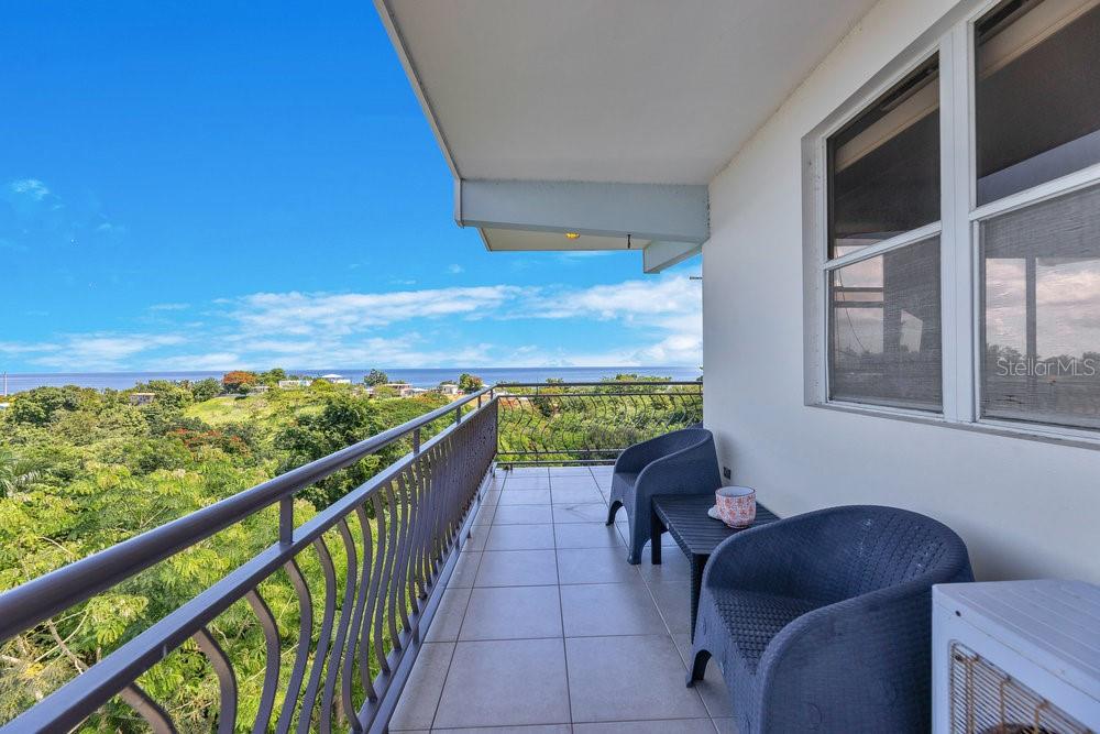 A balcony with tiled flooring, metal railings, and two blue chairs overlooking a coastal view — 413 CAM. CARRETAS UNIT A7, RINCON, PR