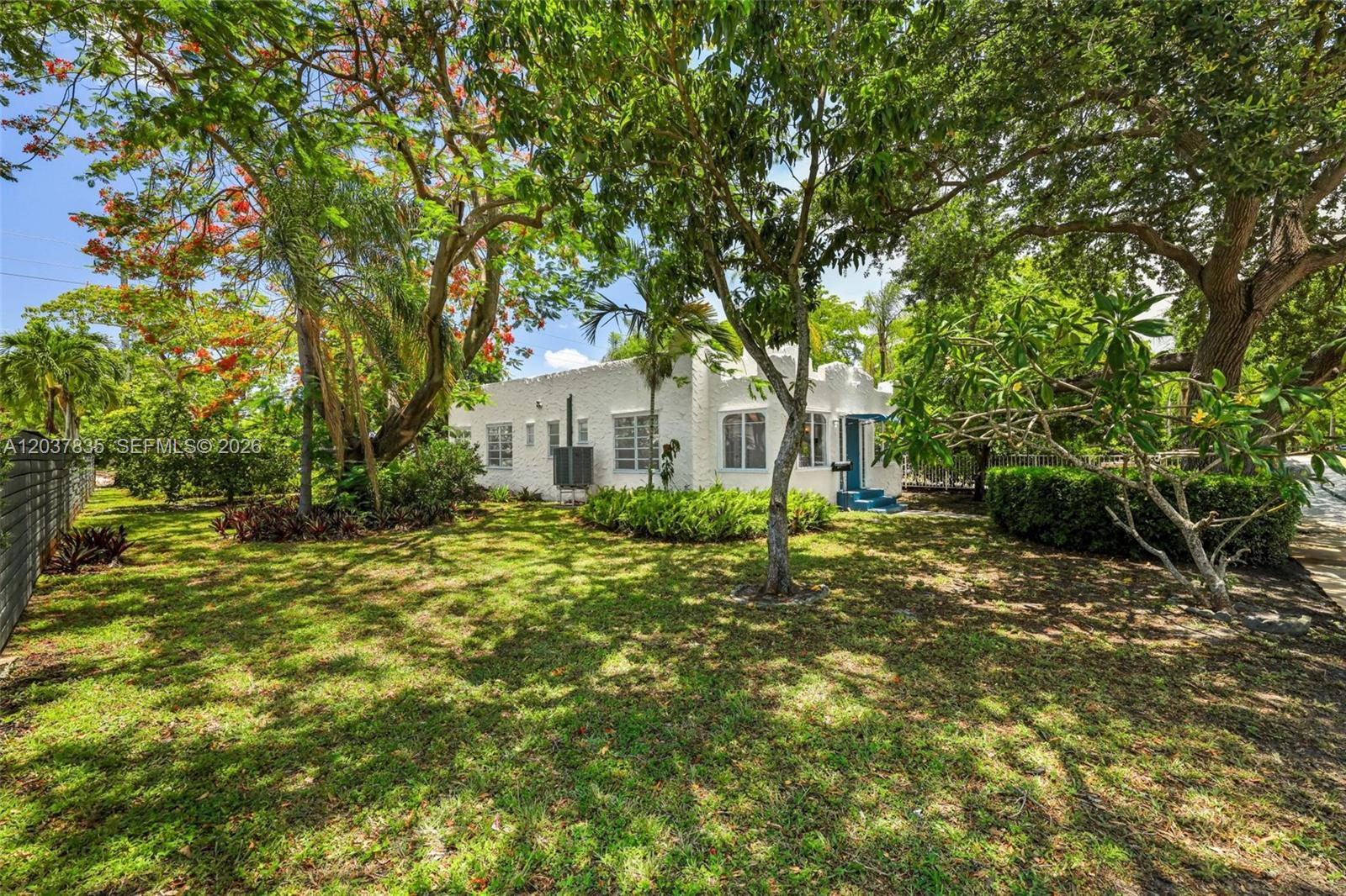 A white, single-story house with a textured exterior sits in a large, tree-shaded yard — 1954 Dewey St, Hollywood FL 33020, HOLLYWOOD, FL