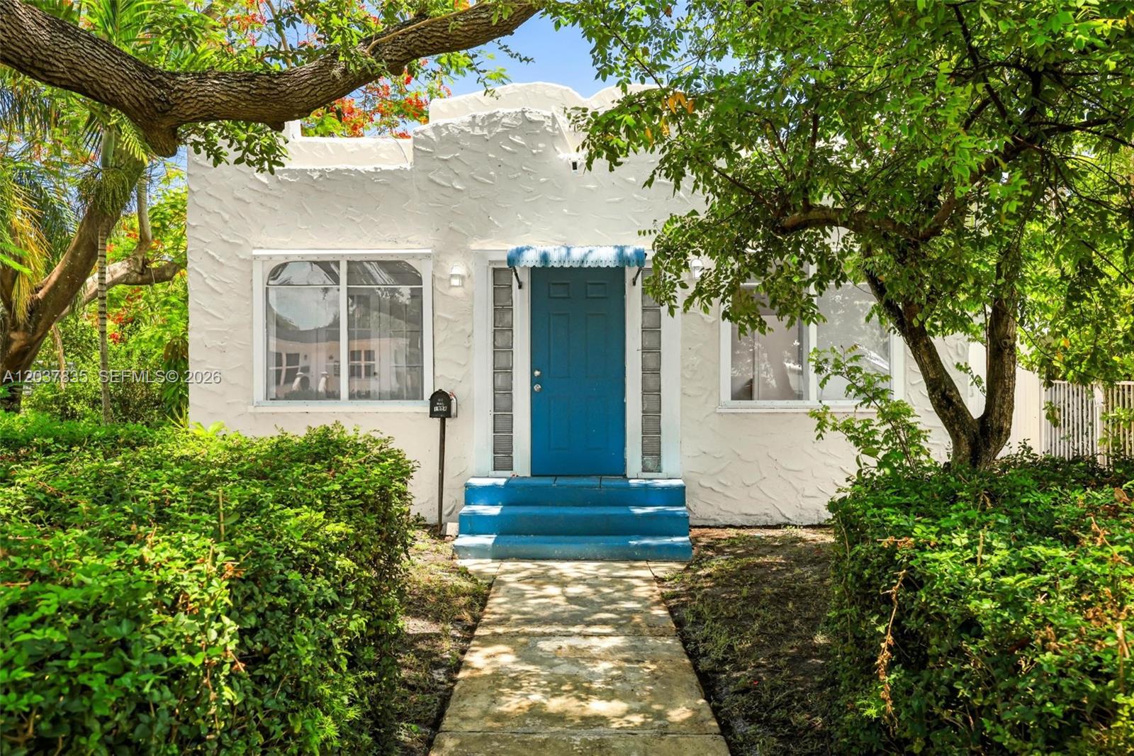 A white stucco house features a blue front door, matching steps, and a small awning — 1954 Dewey St, Hollywood FL 33020, HOLLYWOOD, FL