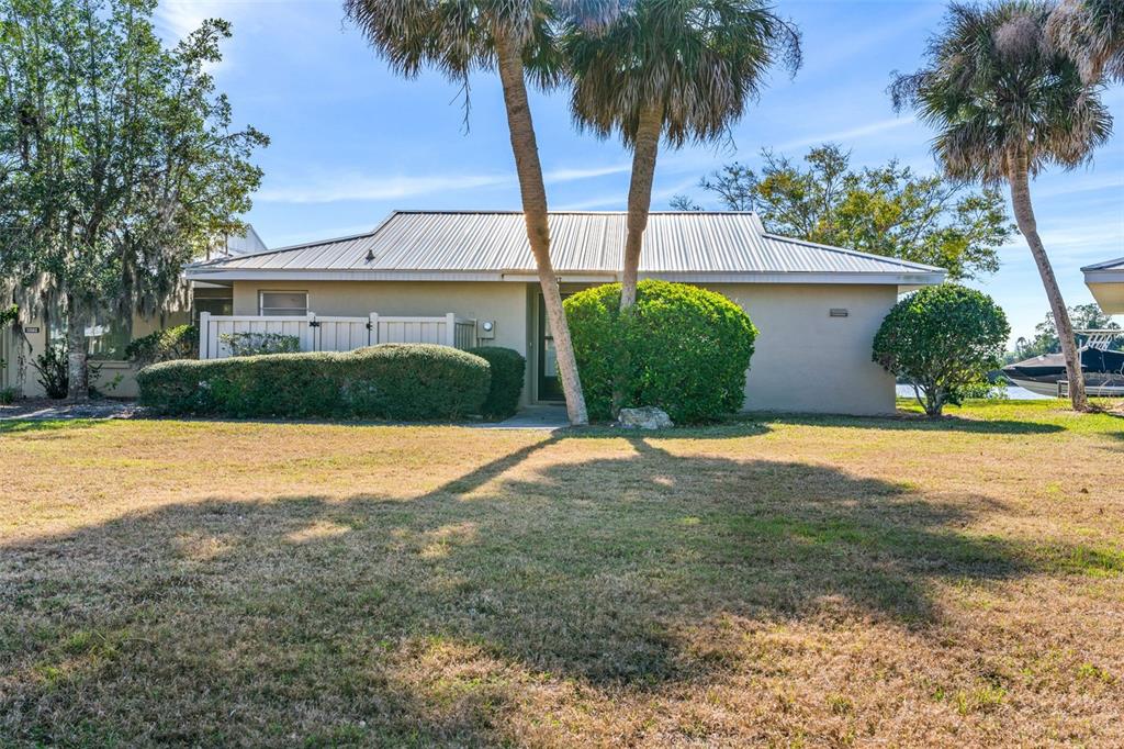 A single-story house with a metal roof, palm trees, and a lawn under a blue sky — 11568 W BAYSHORE DRIVE UNIT 17, CRYSTAL RIVER, FL