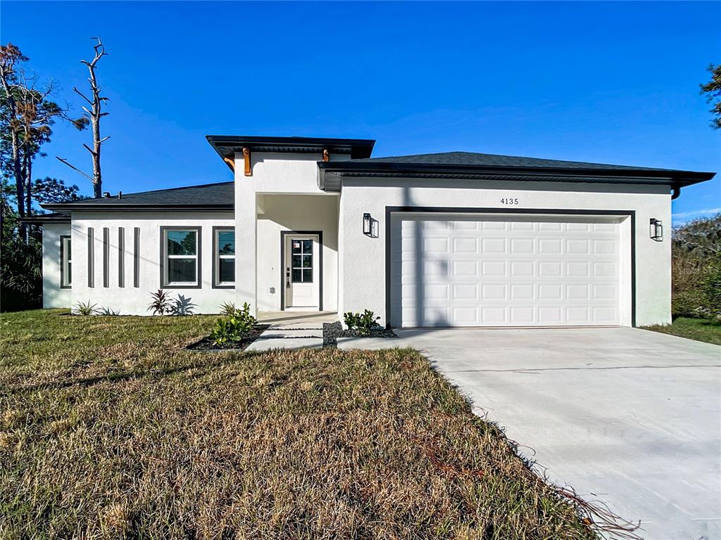 A white single-story house with a two-car garage and a modern entryway under a clear sky — 422 EISENHOWER BOULEVARD, LEHIGH ACRES, FL