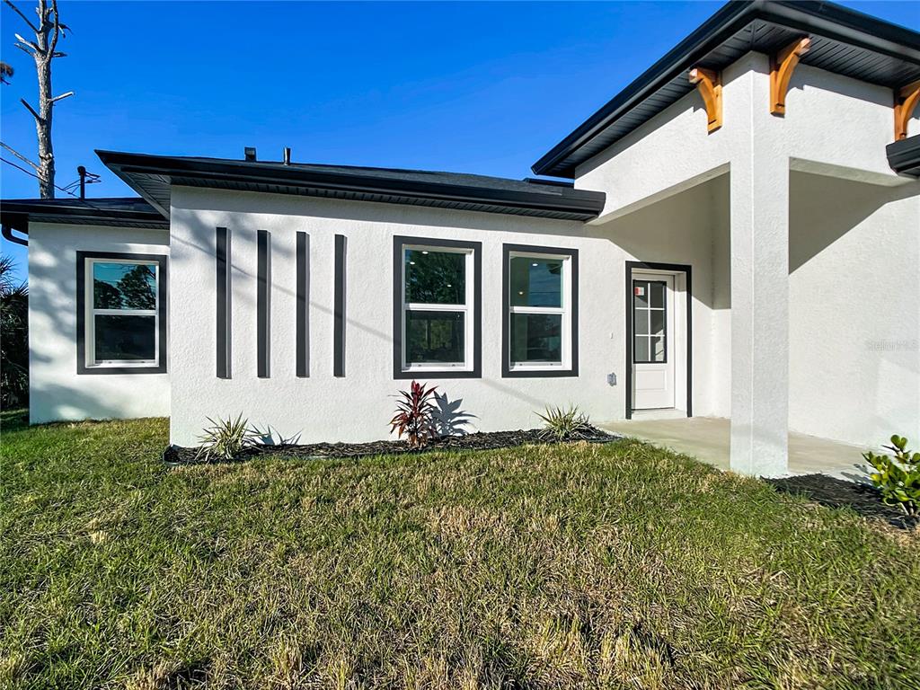 A white stucco house exterior features black window frames, vertical decorative slats, and a covered entryway — 422 EISENHOWER BOULEVARD, LEHIGH ACRES, FL