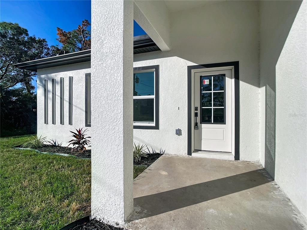 A white stucco house exterior features a covered entryway, a glass-paneled door, and vertical accents — 422 EISENHOWER BOULEVARD, LEHIGH ACRES, FL